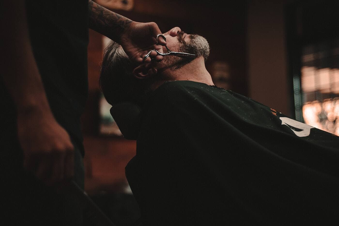 A barber trimming a customer's beard in a traditional barbershop
